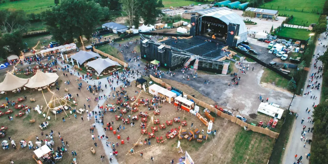 Vista aérea de un festival al aire libre con un gran escenario, carpas, puestos de comida y mucha gente disfrutando del summerfest Cerdanya.