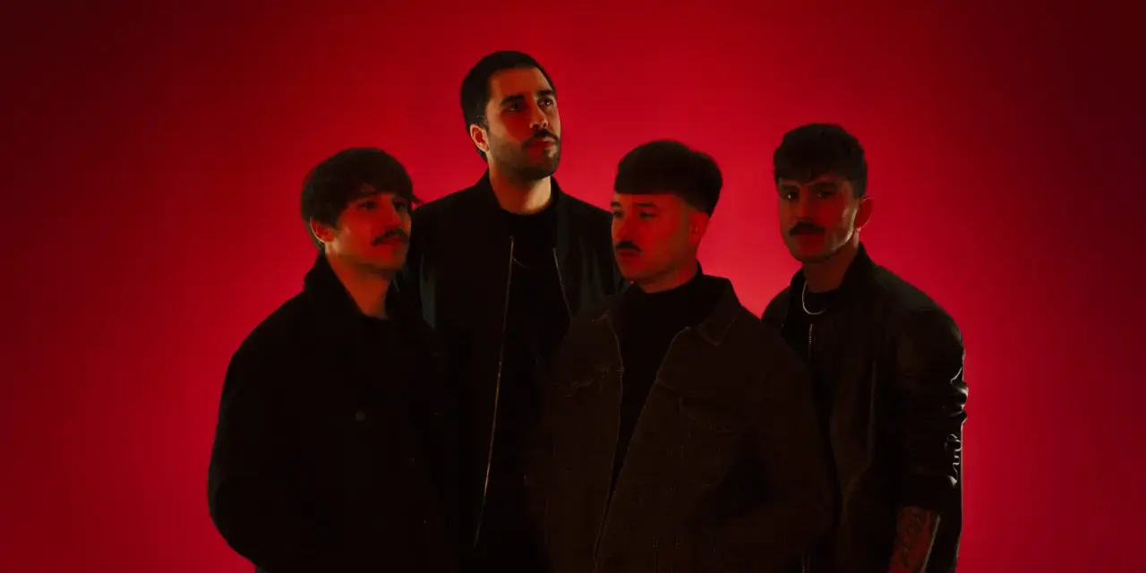 Cuatro hombres posan ante un fondo rojo vibrante. Parecen una banda, quizás "los flamingos", con sus miradas intensas y atuendos modernos.
