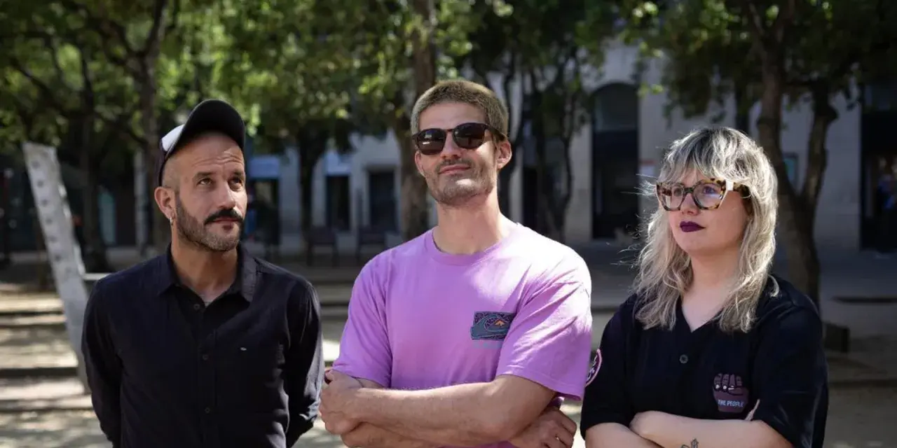 Miembros de Els Catarres posan al aire libre. El hombre de la izquierda lleva gorra y camisa negra. El del centro, gafas de sol y camiseta lila. La mujer de la derecha, gafas y camiseta negra.