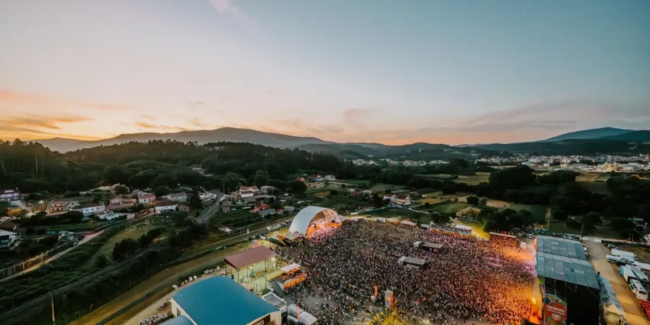 Multitudinaria **rio verbena fest** bajo un atardecer espectacular. Miles de personas disfrutan de la música y el ambiente.