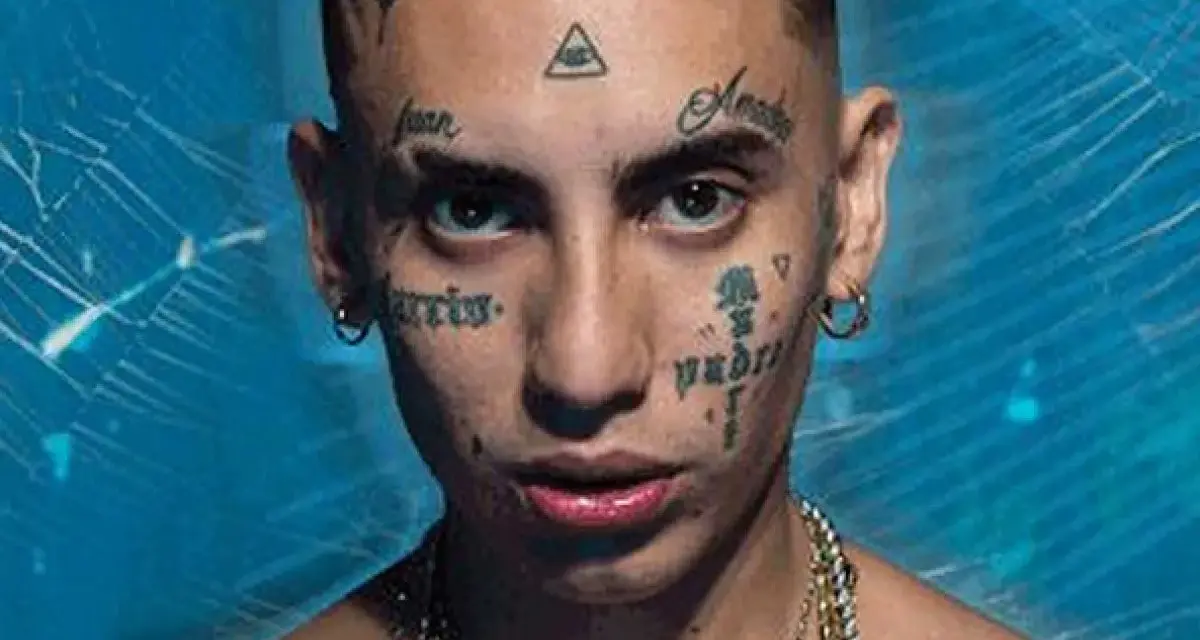 Joven con tatuajes en la cara, incluyendo un ojo dentro de un triángulo, y cadenas de oro. Su estilo neo pistea madrid es inconfundible.