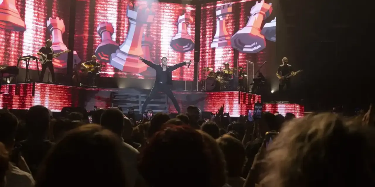 Un cantante en el escenario del 101 music festival, con una pantalla gigante de ajedrez de fondo.