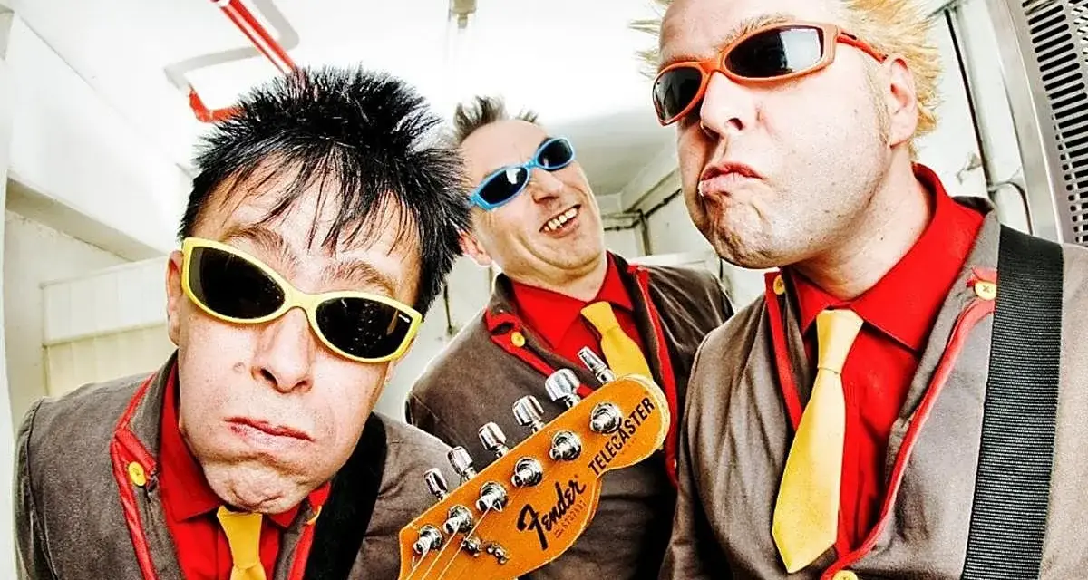 Tres músicos con gafas de sol y trajes coloridos, listos para un concierto de mondra roll.