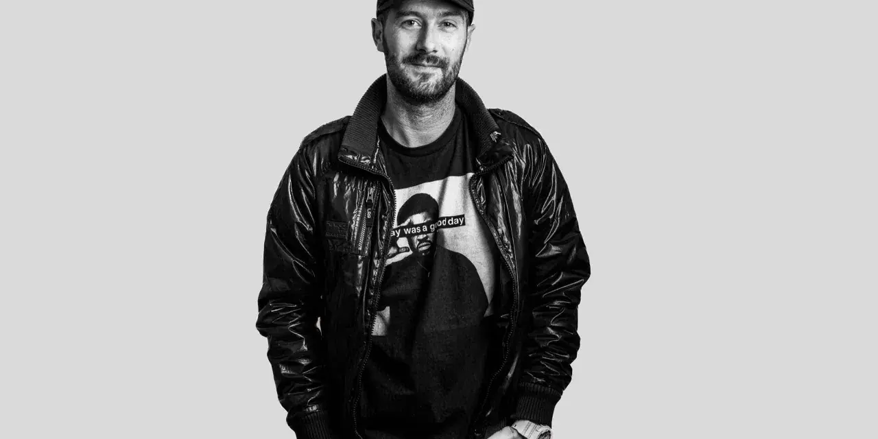 DJ Plan B, con gorra y chaqueta de cuero, sonríe con una camiseta que dice "Today was a good day".