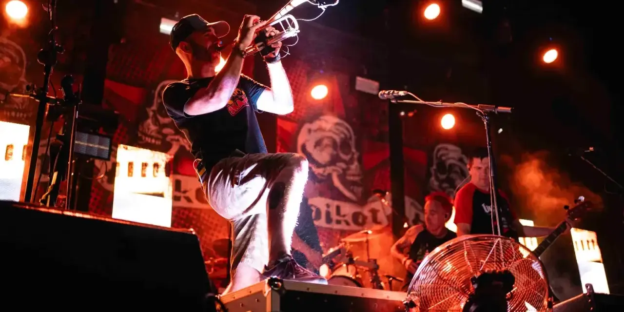 Músico con trompeta en un concierto de soria rock, con luces rojas y fondo de calaveras.