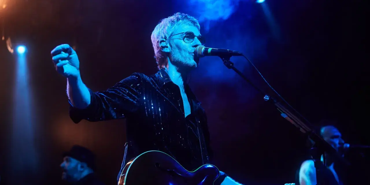 Cantante de Belako en concierto, con guitarra y micrófono, bajo luces azules y humo.