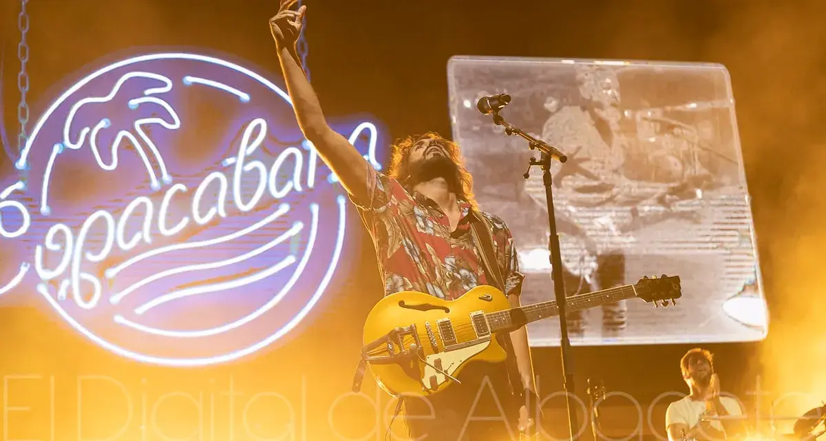 El cantante de Izal en Albacete levanta la mano con su guitarra amarilla, iluminado por un neón de Copacabana.