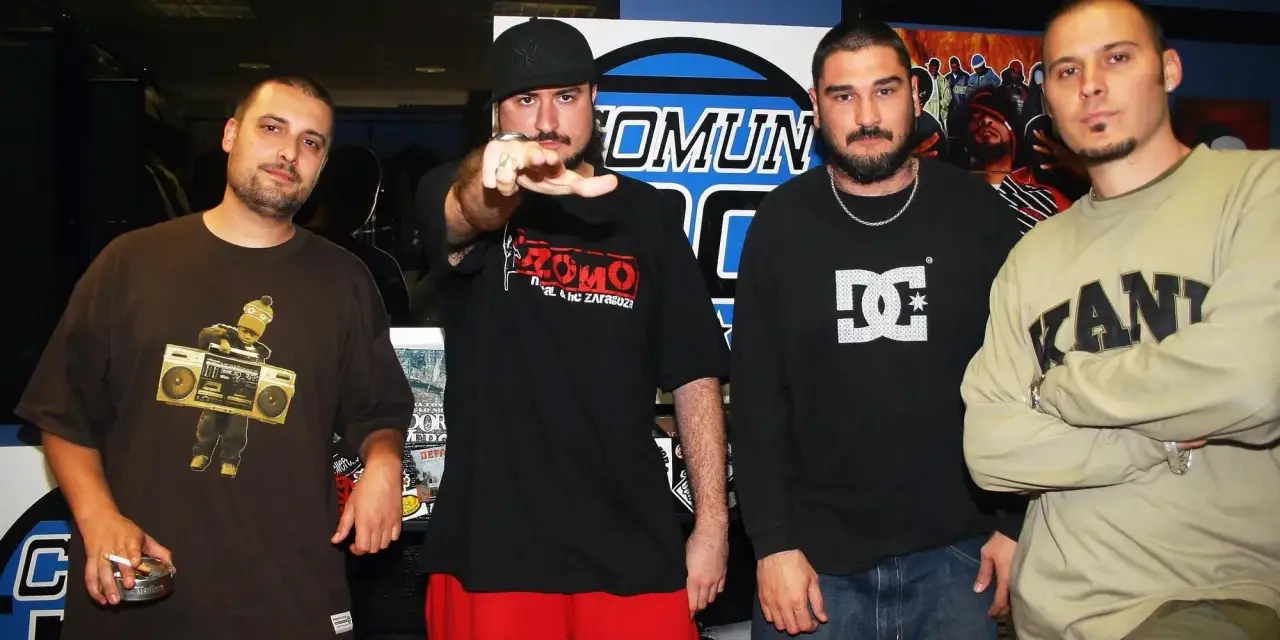 Miembros de Violadores del Verso posan juntos. El rapero de la izquierda lleva una camiseta marrón con un dibujo de un niño con un boombox.