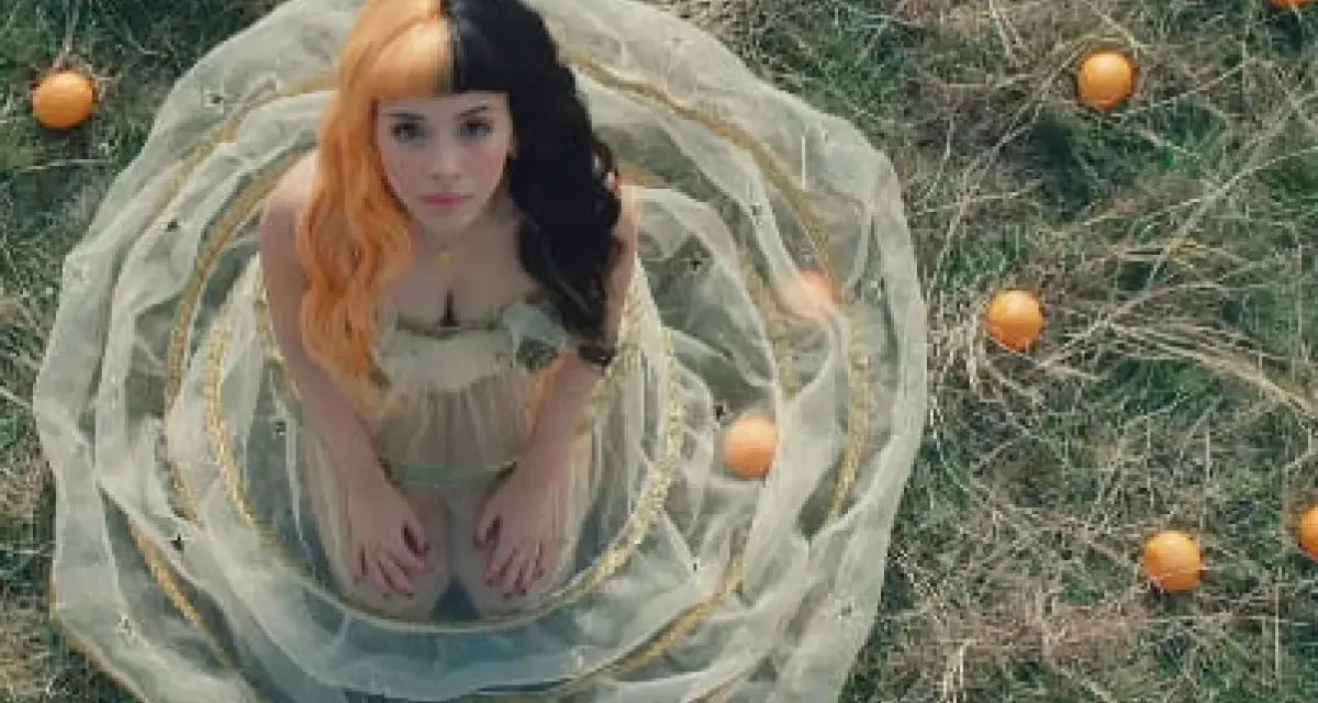 Melanie Martinez, con su icónico cabello mitad naranja y mitad negro, rodeada de naranjas en un campo. ¡Atentos a los próximos eventos de Melanie Martinez!