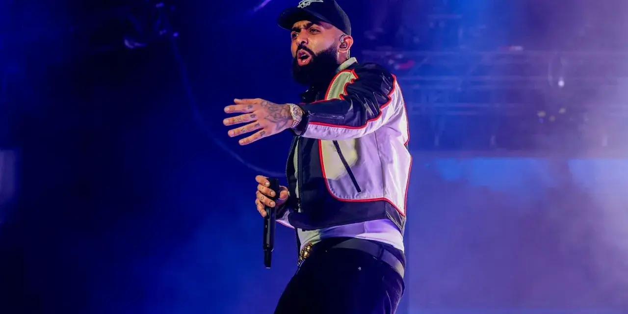 Nicky Jam, con su gorra y chaqueta llamativa, canta en un concierto en Granada, cautivando al público con su energía.