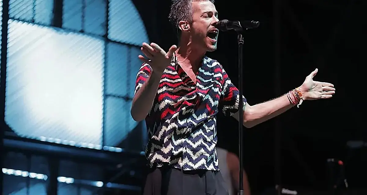 El cantante de Vetusta Morla Sevilla canta apasionadamente en un concierto, con las manos extendidas y un micrófono frente a él.