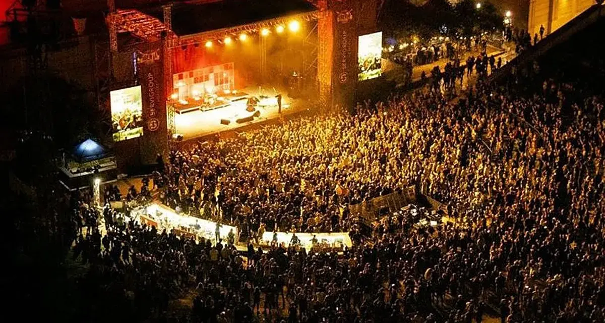 Multitudinaria asistencia a conciertos en julio. Una banda toca en un escenario iluminado ante miles de fans.