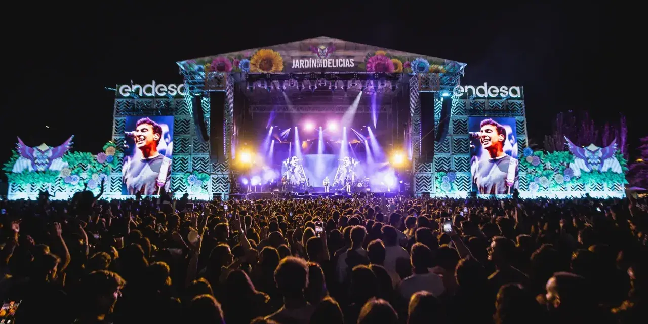 Gran concierto en el Jardín de las Delicias. Multitud vibrante ante el escenario iluminado, con pantallas gigantes mostrando al artista.