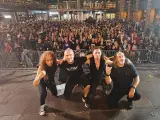 La banda Syberia posa con su público. Los músicos, con atuendos oscuros, se arrodillan mientras una multitud enardecida los aclama.