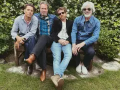 Un grupo de cuatro hombres con ropa informal sentados en un banco, todos con una gran sonrisa.