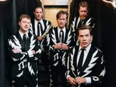 Los miembros de The Hives posan con trajes llamativos. Uno sostiene baquetas, listo para la acción.