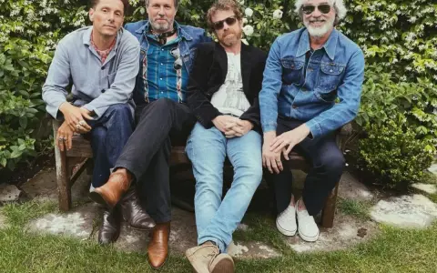 Un grupo de cuatro hombres con ropa informal sentados en un banco, todos con una gran sonrisa.