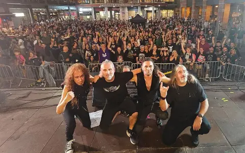 La banda Syberia posa con su público. Los músicos, con atuendos oscuros, se arrodillan mientras una multitud enardecida los aclama.