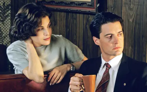 Una mujer y un hombre en una noche sin grabar. Él sostiene una taza de café, ella apoya la cabeza en la mano.