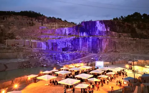 Un impresionante festival Porriño ilumina una cantera con luces moradas. Gente reunida bajo sombrillas blancas, disfrutando del evento.