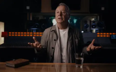 Jim Kerr, uno de los miembros de Simple Minds, habla en un estudio de grabación, con un libro y un vaso de agua sobre la mesa.