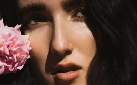 Primer plano de Judeline, cantante, con una flor rosa junto a su rostro.