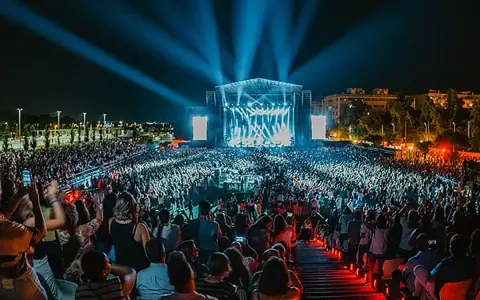 Multitud en un concierto nocturno, luces azules iluminan el escenario y al público. Un evento vibrante, como un **cabaret mairena** moderno.