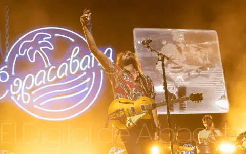El cantante de Izal en Albacete levanta la mano con su guitarra amarilla, iluminado por un neón de Copacabana.