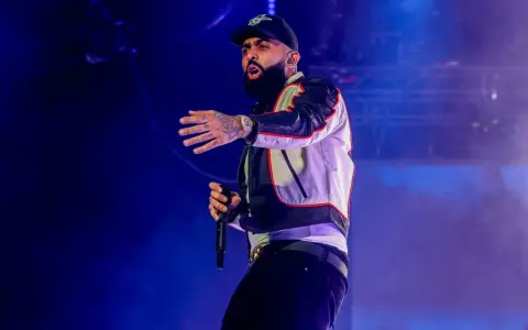 Nicky Jam, con su gorra y chaqueta llamativa, canta en un concierto en Granada, cautivando al público con su energía.