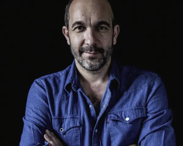 Hombre con barba y camisa vaquera azul, mirada directa. Podría ser DJ Coco listo para pinchar.