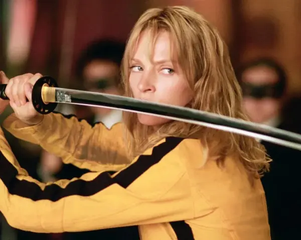 La Novia, con su icónico traje amarillo, desenvaina su katana. La banda sonora de Kill Bill resuena en esta escena de acción.