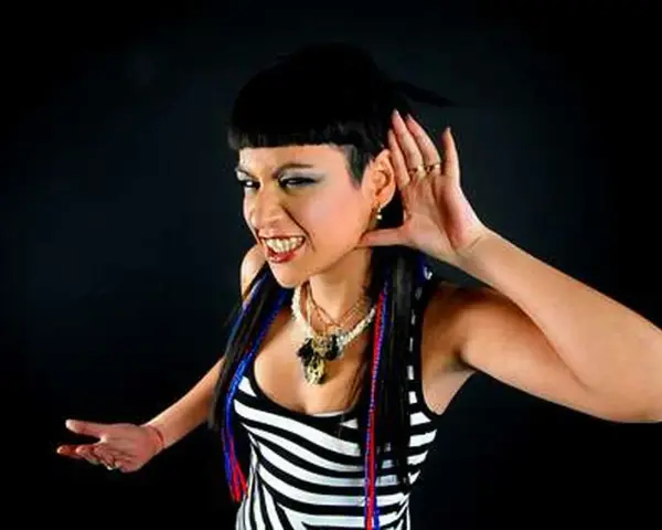 Fatima Hajji, con su característico estilo, escucha atentamente, con una mano en la oreja y una sonrisa pícara.