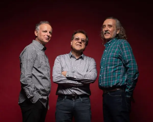 Los miembros de Els Pets posan sonrientes ante un fondo rojo.