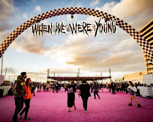 Gente camina bajo un arco con el letrero "When We Were Young Festival" sobre una alfombra rosa.