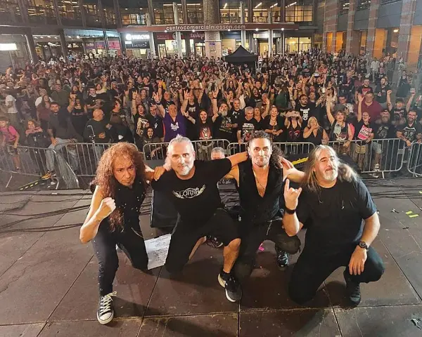 La banda Syberia posa con su público. Los músicos, con atuendos oscuros, se arrodillan mientras una multitud enardecida los aclama.