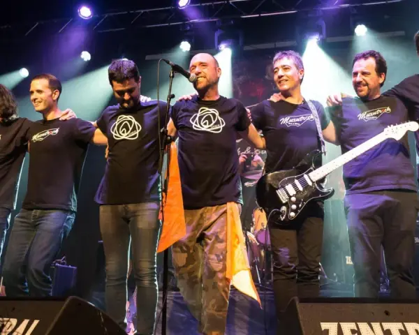 Seis músicos de maizu rock en el escenario, abrazados y sonriendo. Uno sostiene una guitarra eléctrica.