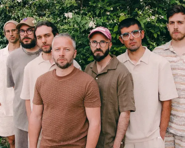 Los miembros de Oques Grasses posan juntos, con ropa de tonos tierra y un fondo de vegetación frondosa.