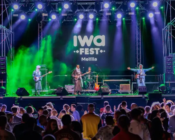 Banda tocando en el iwa fest de Melilla, con luces verdes y moradas, y una multitud disfrutando.