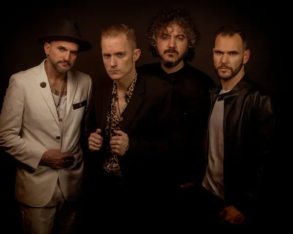 El grupo de embusteros posa con miradas intensas. Uno lleva sombrero y traje blanco, otro camisa de leopardo, y los otros dos, chaquetas oscuras.