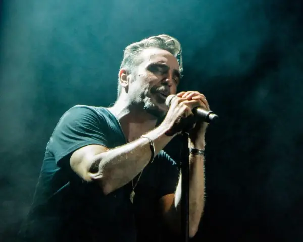 Un miembro de OBK canta apasionadamente en el escenario, iluminado por focos.