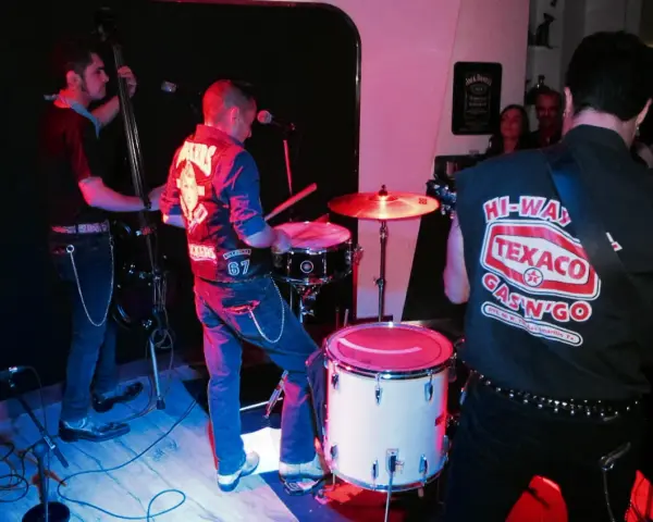 Un grupo de gatos locos en el escenario, tocando rock and roll con un contrabajo, batería y guitarra.