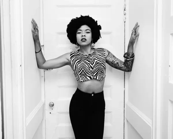 Nikki Hill, con su afro y top de cebra, posa con confianza entre puertas blancas.