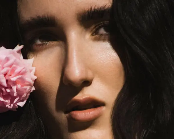 Primer plano de Judeline, cantante, con una flor rosa junto a su rostro.