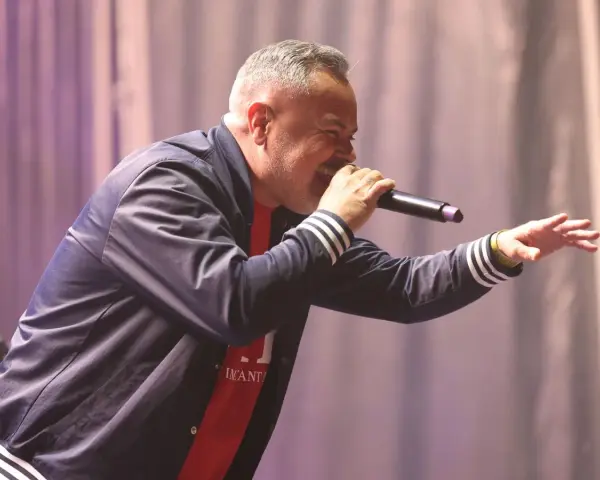 Juan Magán cantando en un escenario con micrófono y gesto animado.