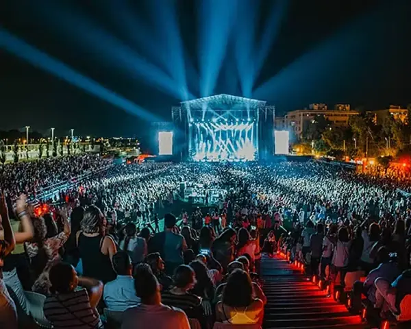 Gran concierto nocturno con multitud de público frente a un escenario iluminado con luces azules.