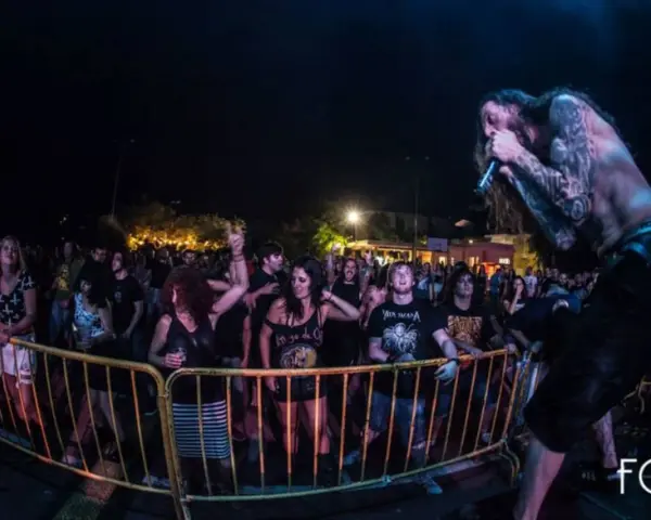Un cantante con tatuajes canta en un concierto de charca rock. El público, animado, se agolpa tras una valla amarilla.