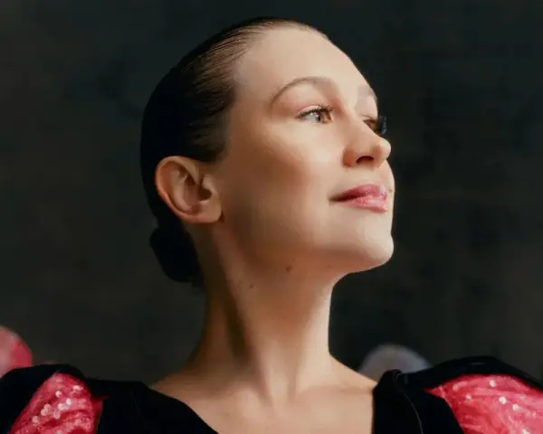 Joanna Newsom, con su cabello recogido y un vestido negro con detalles brillantes, mira hacia arriba con una expresión serena.