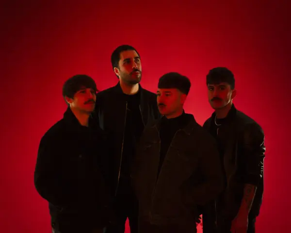 Cuatro hombres posan ante un fondo rojo vibrante. Parecen una banda, quizás "los flamingos", con sus miradas intensas y atuendos modernos.