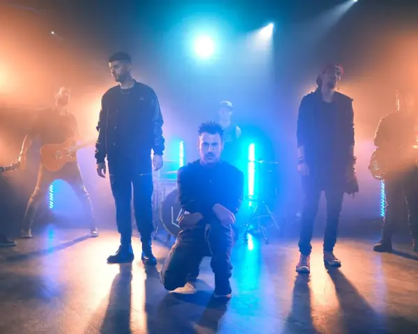 Banda de rock en escenario con luces azules y naranjas, como si estuvieran en un concierto de Linkin Park en Barcelona.