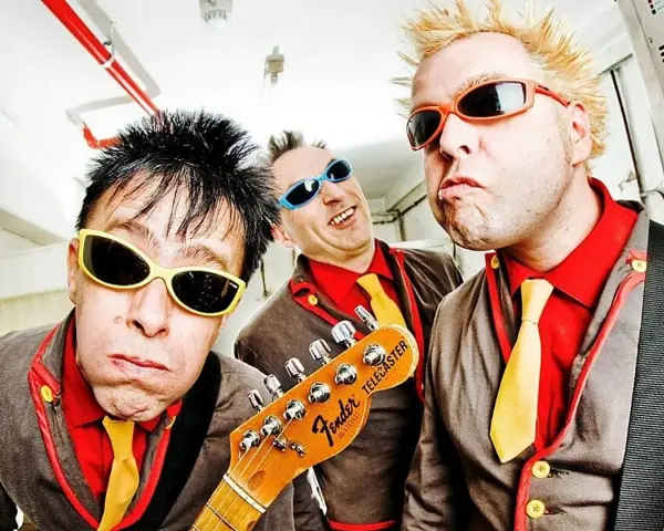 Tres músicos con gafas de sol y trajes coloridos, listos para un concierto de mondra roll.
